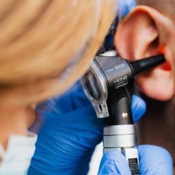 A hand holding an otoscope into an ear.